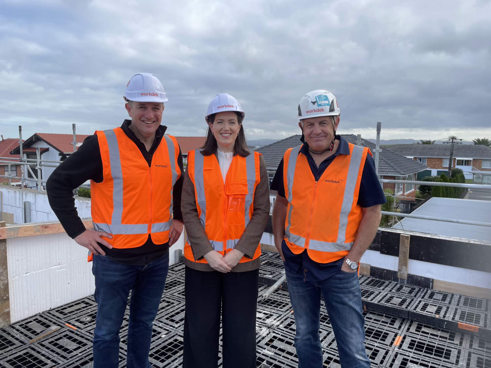 Three Workdek team members in orange hi-vis vests and white hard hats standing on a Workdek platform at a construction site