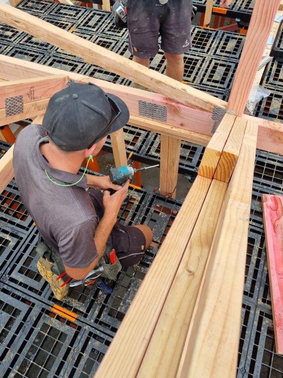 Builder kneeling on a Workdek panel using an impact driver on roof framing