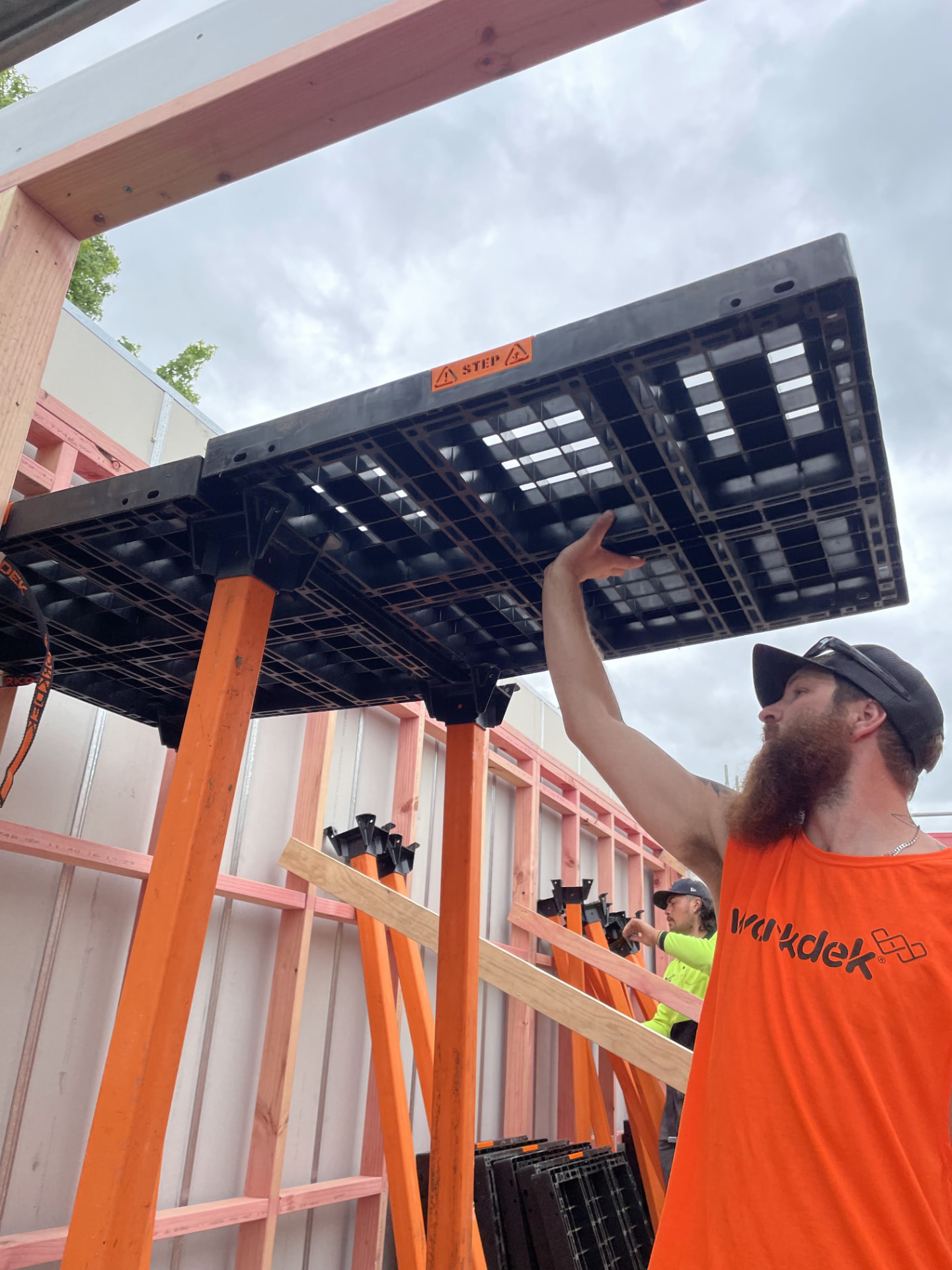 Two installers lifting a Workdek panel into place above orange legs