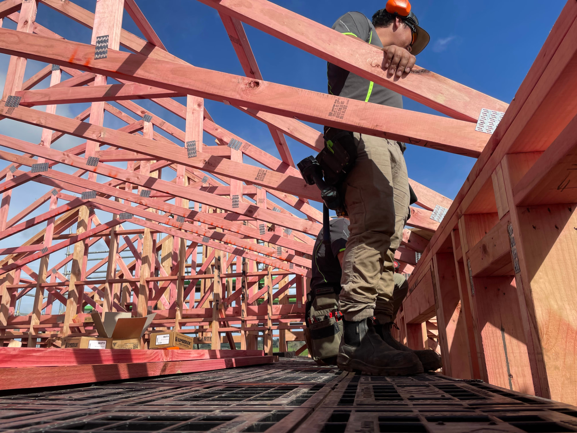 Builder carrying a length of timber across a Workdek platform under a timber roof frame