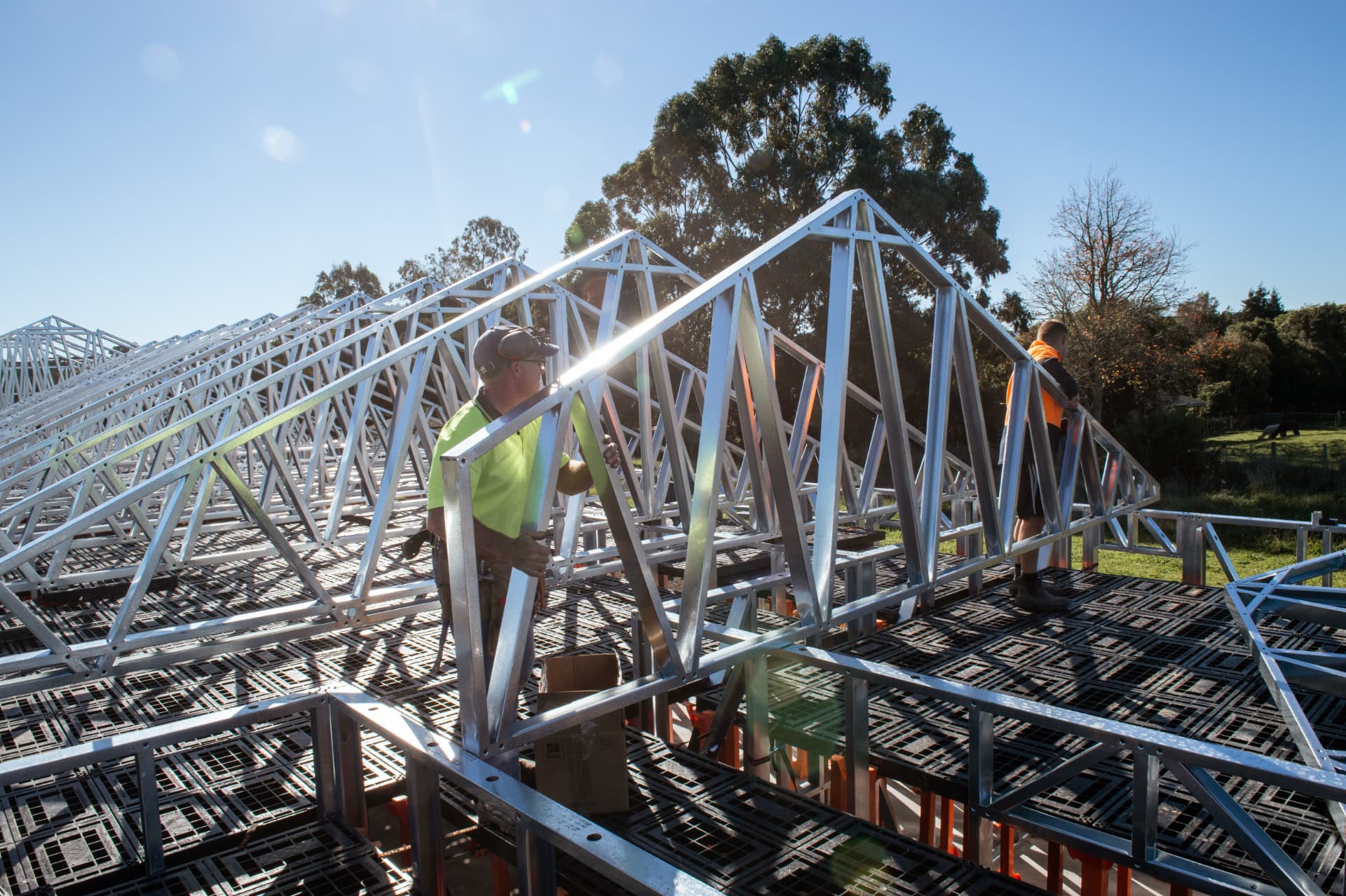Two builders lifting a steel roof truss while standing on a continuous Workdek platform